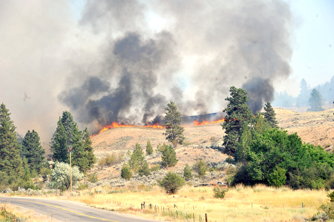 Fire can be seen from the Oroville-Chesaw Road as flames crest a hill burning in dry grasses and sage Thursday. Gary DeVon/staff photos 