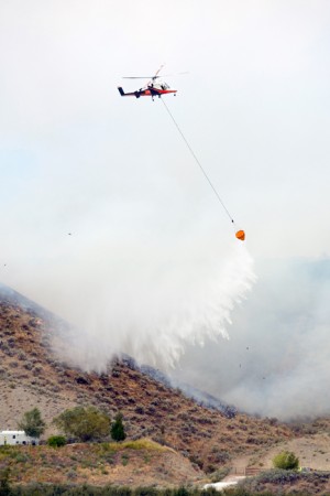Phil Melton, flying the Team HeliQwest K-Max, dumps water over a ridge of flames close to homes near McLaughlin Canyon Aug. 21. Katie Teachout/staff photo