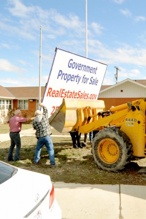 Rod Noel uses a front end loader to pull the Property for Sale sign  from the ground and Councilman Hart and  Brad Calico help with the sign removal.