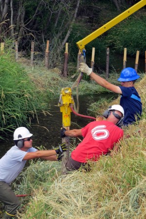 Triple Creek team members and helper install a beaver dam analogue post using a pneumatic hammer.