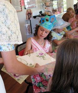 Photo by Amy Veneziano	With her crown complete, one little girl picks out the perfect paper for a hand fan from helper Mishara, 13 years old.