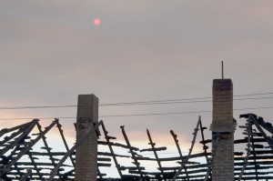 The burned roof of the house, with smoke from the Newby Lake fire darkening the sky behind them.