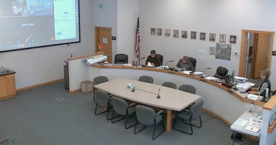 The Okanogan County Commissioners met Tuesday, March 28 and opened the bids for the contact to publish the county’s legal advertising at 10:30 a.m. Seated are, l-r, Commissioner Jon Neal, Commissioner Andy Hover and Clerk of the Board Lanie Johns. Chris Branch, chairman of the Board of Commissioners, who met via Zoom, can be seen on the screen on the wall to the left. The commissioners awarded the bid to be shared by the Okanogan Valley Gazette-Tribune and the Methow Valley News. <sub><em>Zoom Screen Capture </em></sub>