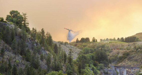 A plane drops water on hot spots along the Similkameen River last Saturday evening. The Eagle Bluff Fire, which began near Blue Lake Road spread quickly northward pushed by winds, eventually jumping the border into Canada. <em>Gary DeVon/staff photo </em>