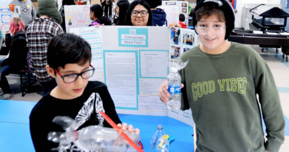 Alredo Alejandre winds up a twin rubber band powered model sub made from a plastic bottle. He was paired up with Choice High School student brandi Rodriguez pon a project titled do submarines need fins. Aslo pictured is fifth-grader Rowan Jones. <em>Gary DeVon/staff photos </em>