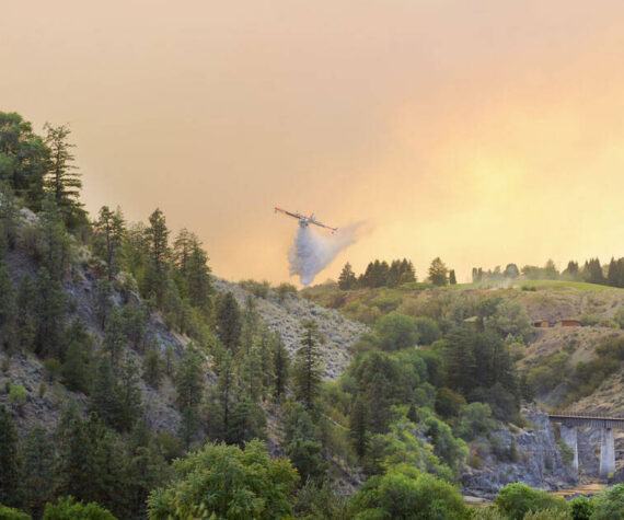 A plane drops water on hot spots along the Similkameen River last Saturday evening. The Eagle Bluff Fire, which began near Blue Lake Road spread quickly northward pushed by winds, eventually jumping the border into Canada. <em>Gary DeVon/staff photo</em>