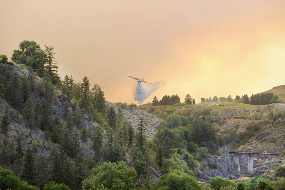 A plane drops water on hot spots along the Similkameen River last Saturday evening. The Eagle Bluff Fire, which began near Blue Lake Road spread quickly northward pushed by winds, eventually jumping the border into Canada. <em>Gary DeVon/staff photo</em>