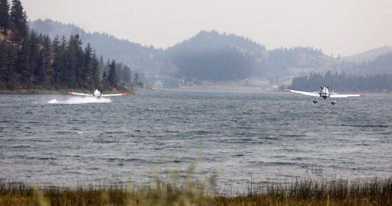 Two water-bomber planes gather water from Wannacut Lake to fight flames at the Rainbow Lake Fire on Palmer Mountain and the Wannacut Fire. The Rainbow Lake Fire was listed at 150 acres on Tuesday afternoon and the Wannacut lake fire was listed at 64 acres. Smoke from these fires and larger fires in the Methow, Chelan and lower British Columbia areas has settled in the Okanogan Valley. <em>Laura Knowlton/staff photo </em>