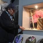 Lewis points to a display case featuring cxelusa bulbs, a hand-woven basket, and a traditional puca made of wood and a piece of antler at the Colville Tribal Museum in Grand Coulee, Wash. on Saturday, April 22, 2023. (Dominick Bonny for Crosscut)